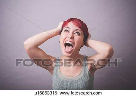 Stock Photography - Studio portrait of young woman with hands in hair shouting. Fotosearch