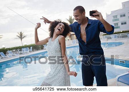 Stock Photography - "Stylish couple taking dance smartphone selfie at hotel poolside, Rio De Janeiro, Brazil". Fotosearch