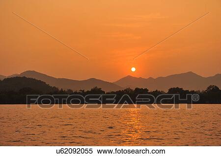 Stock Photography - "Sunset over lake, mountains in distance, Hangzhou, China". Fotosearch
