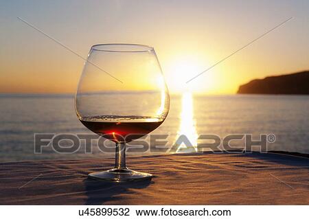 Stock Image - "Sunset over sea with brandy glass on table, Mallorca, Spain". Fotosearch