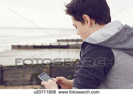 "Teenage boy at seaside texting on smartphone, Southend on Sea, Essex, UK" View Large Photo Image Stock Photo - "Teenage boy at seaside texting on smartphone, Southend on Sea, Essex, UK". Fotosearch