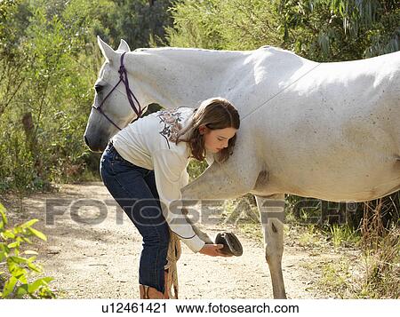 Stock Image - Teenage girl checking horse hoof. Fotosearch