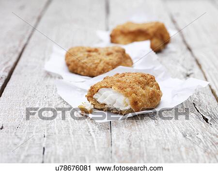 Stock Image - Three fried breaded chunky cod pieces on wooden table. Fotosearch
