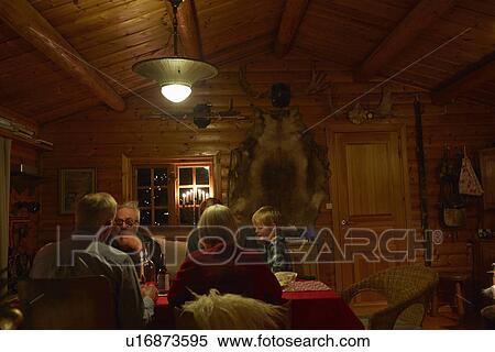 Stock Photography - Three generation family sitting talking at Christmas table in log cabin at night. Fotosearch