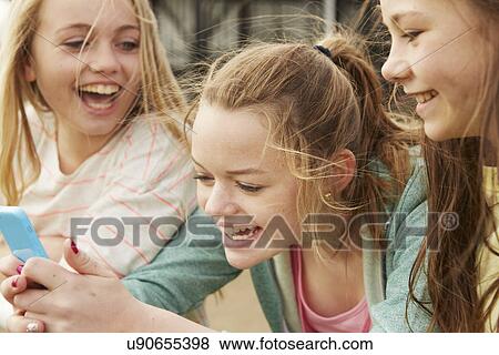 Three girls laughing at smartphone text View Large Photo Image Stock Photo - Three girls laughing at smartphone text. Fotosearch