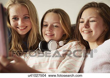 Picture - Three girls on sofa using digital tablet. Fotosearch