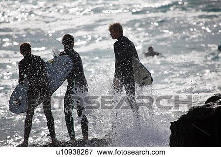 Stock Photo - "Three silhouetted male surfers standing on sea rocks, Fuerteventura, Spain". Fotosearch
