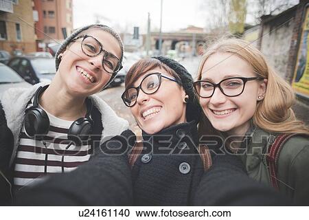 Stock Image - Three sisters taking selfie on street. Fotosearch