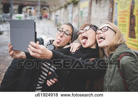 Stock Photo - Three sisters taking selfie on street. Fotosearch