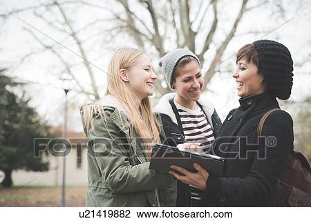 Stock Image - Three sisters using digital tablet in park. Fotosearch