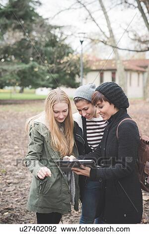Three sisters using digital tablet in park View Large Photo Image Stock Image - Three sisters using digital tablet in park. Fotosearch