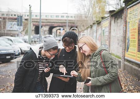 Stock Image - Three sisters using digital tablet on street. Fotosearch