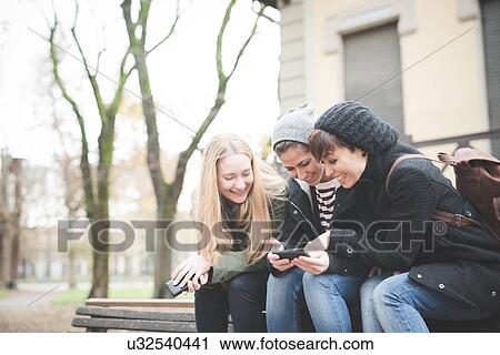 Three sisters using smartphone on park bench View Large Photo Image Stock Image - Three sisters using smartphone on park bench. Fotosearch