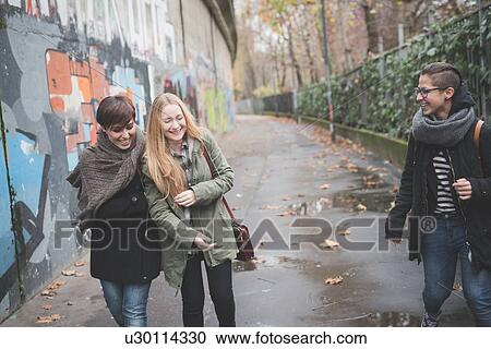 Stock Image - Three sisters walking by graffiti wall. Fotosearch