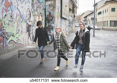 Stock Image - Three sisters walking by graffiti wall. Fotosearch