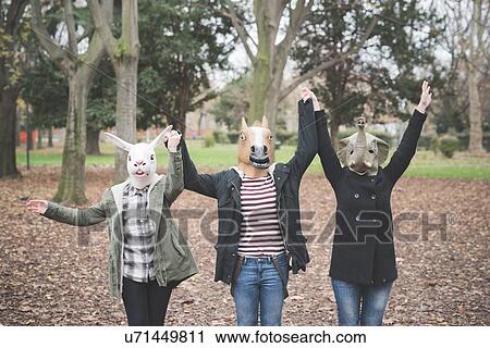 Stock Image - Three sisters wearing animal masks dancing in park. Fotosearch