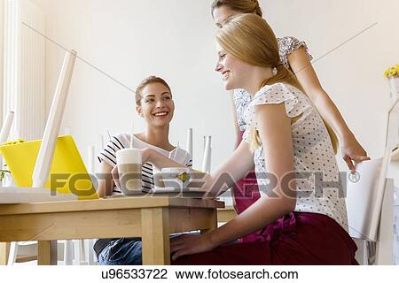 Stock Image - Three women using laptop in cafe. Fotosearch