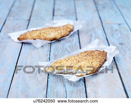Stock Image - Two fried breaded flounder fish pieces on wooden table. Fotosearch