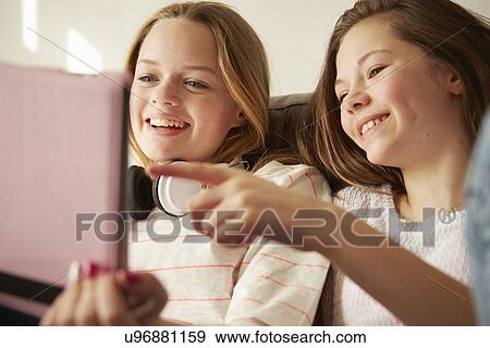 Two girls on sofa laughing and pointing at digital tablet View Large Photo Image Stock Photo - Two girls on sofa laughing and pointing at digital tablet. Fotosearch