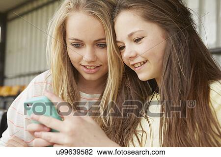 Two girls reading smartphone texts in shelter View Large Photo Image Stock Image - Two girls reading smartphone texts in shelter. Fotosearch