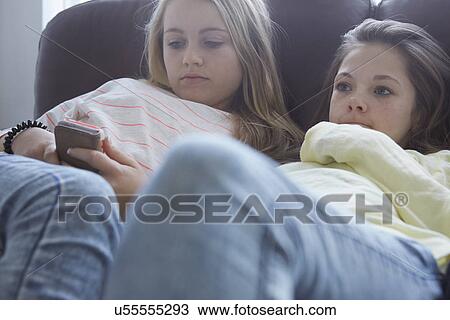 Two girls watching tv and smartphone texting on sofa View Large Photo Image Stock Image - Two girls watching tv and smartphone texting on sofa. Fotosearch