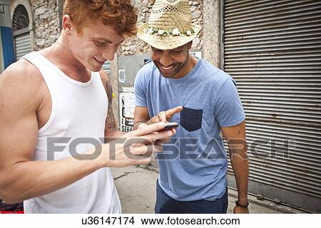 Picture - Two male friends looking at smartphone together. Fotosearch