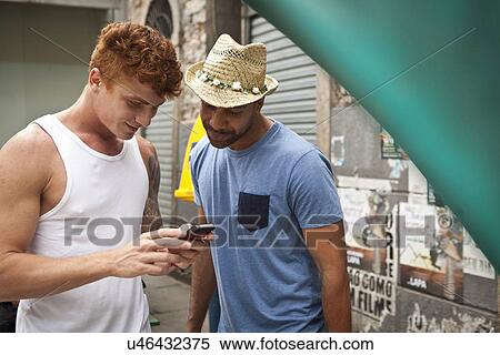 Two male friends looking at smartphone together View Large Photo Image Stock Photography - Two male friends looking at smartphone together. Fotosearch