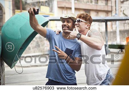 Stock Image - Two male friends taking self portrait using smartphone. Fotosearch