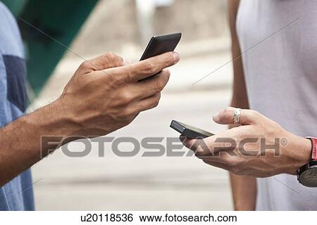 "Two men holding smartphones, focus on hands, close-up" View Large Photo Image Stock Photograph - "Two men holding smartphones, focus on hands, close-up". Fotosearch