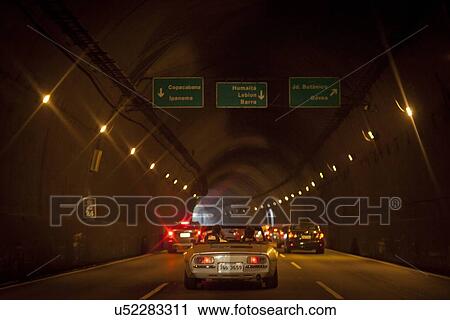 Stock Image - "Two men in convertible car in tunnel, rear view". Fotosearch
