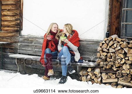 Two young female friends drinking coffee outside wooden cabin View Large Photo Image Picture - Two young female friends drinking coffee outside wooden cabin. Fotosearch