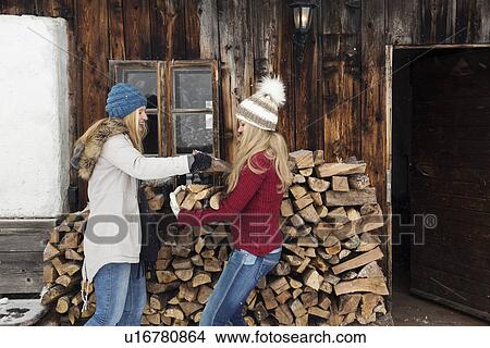 Picture - Two young female friends stacking logs outside cabin. Fotosearch