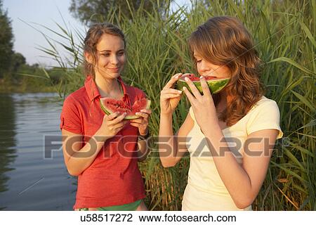 Two young women eating watermelon slices at lakeside View Large Photo Image Stock Image - Two young women eating watermelon slices at lakeside. Fotosearch