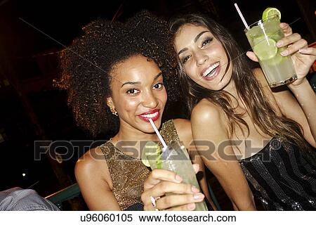 "Two young women in bar, drinking cocktails, looking at camera, smiling" View Large Photo Image Stock Photography - "Two young women in bar, drinking cocktails, looking at camera, smiling". Fotosearch