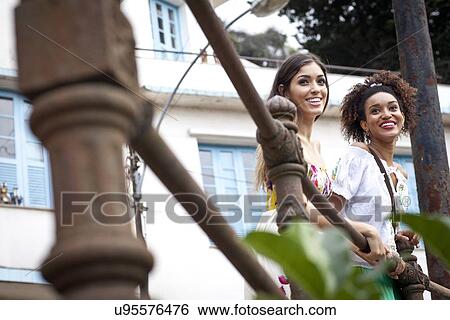 "Two young women standing by railings, low angle view" View Large Photo Image Stock Photograph - "Two young women standing by railings, low angle view". Fotosearch