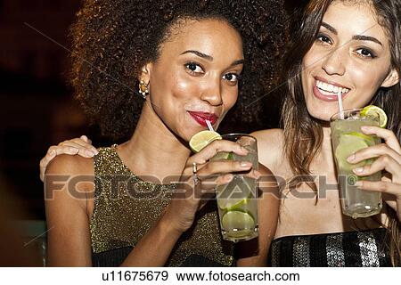 Stock Photo - "Two young women together in bar, drinking, smiling". Fotosearch