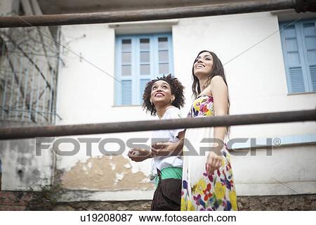 Stock Photo - "Two young women walking along walkway together, low angle view". Fotosearch