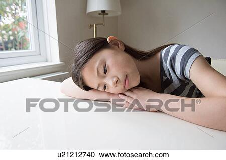 Unhappy girl at table resting on arms View Large Photo Image Stock Image - Unhappy girl at table resting on arms. Fotosearch