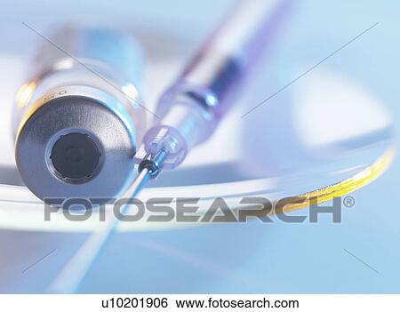 Stock Photograph - Vaccine and hypodermic syringe sitting on a glass dish. Fotosearch