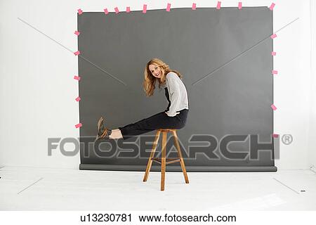 Stock Image - Woman on stool in front of photographers backdrop. Fotosearch