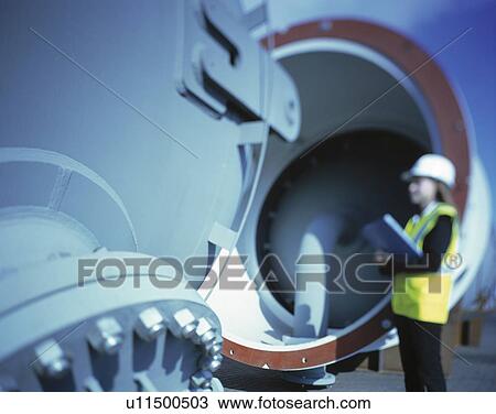 Stock Image - "Worker inspecting pipes in port, Grimsby, England, United Kingdom". Fotosearch