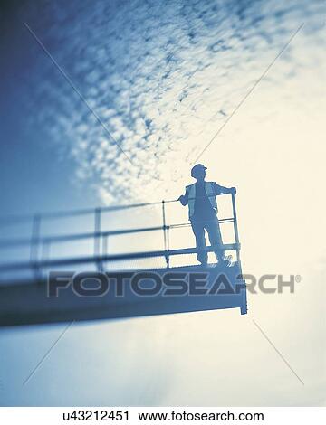 Stock Image - "Worker on crane gantry, low angle view". Fotosearch