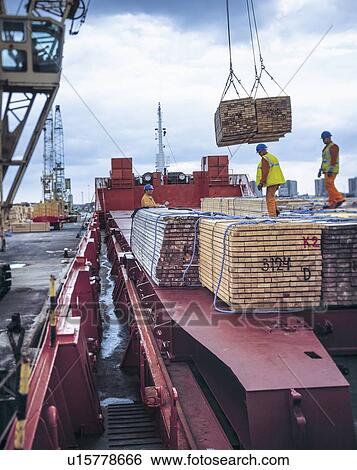 Stock Photograph - "Workers unloading timber from cargo ship in port, Grimsby, England, United Kingdom". Fotosearch