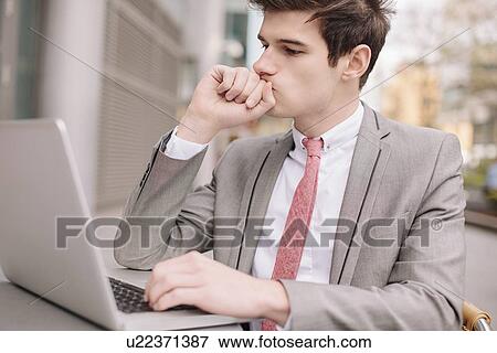 Stock Photo - Worried young city businessman using laptop at sidewalk cafe. Fotosearch