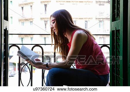 Young adult female sitting on balcony reading View Large Photo Image Picture - Young adult female sitting on balcony reading. Fotosearch