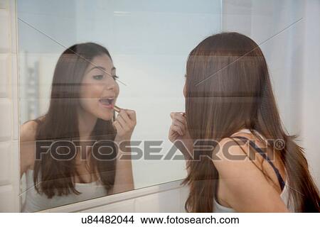 Picture - Young adult woman applying make up in mirror. Fotosearch