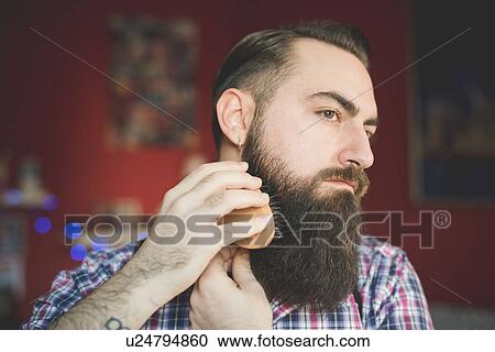 Stock Image - Young bearded man brushing his beard. Fotosearch