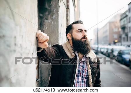 Stock Image - Young bearded man by concrete wall. Fotosearch