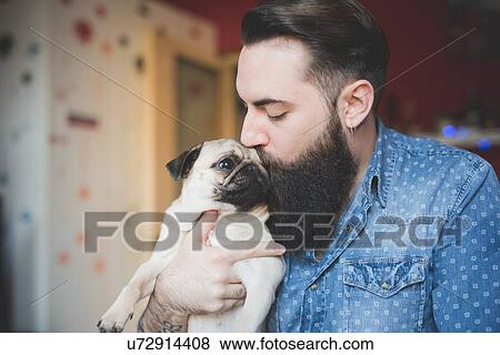 Young bearded man kissing dog in arms View Large Photo Image Stock Photo - Young bearded man kissing dog in arms. Fotosearch