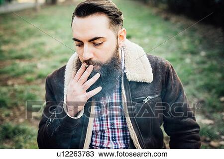 Young bearded man smoking in park View Large Photo Image Stock Image - Young bearded man smoking in park. Fotosearch